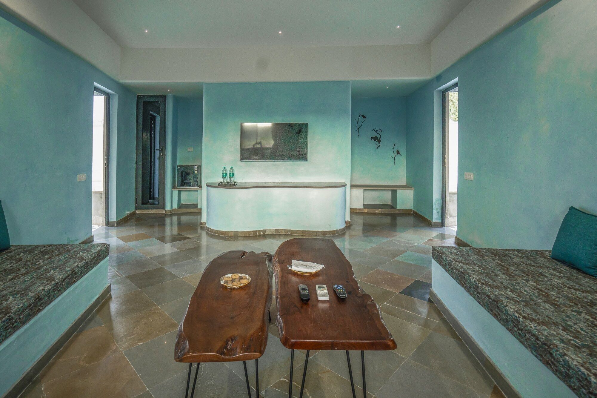 A reception area with a counter, two wooden tables with remote controls, and a seating area with a blue wall and a painting.