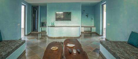 A reception area with a counter, two wooden tables with remote controls, and a seating area with a blue wall and a painting.