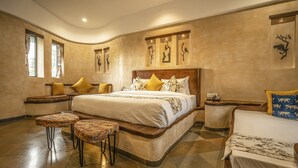Une chambre spacieuse avec un grand lit, deux tables de chevet, un banc et une petite table avec une lampe.