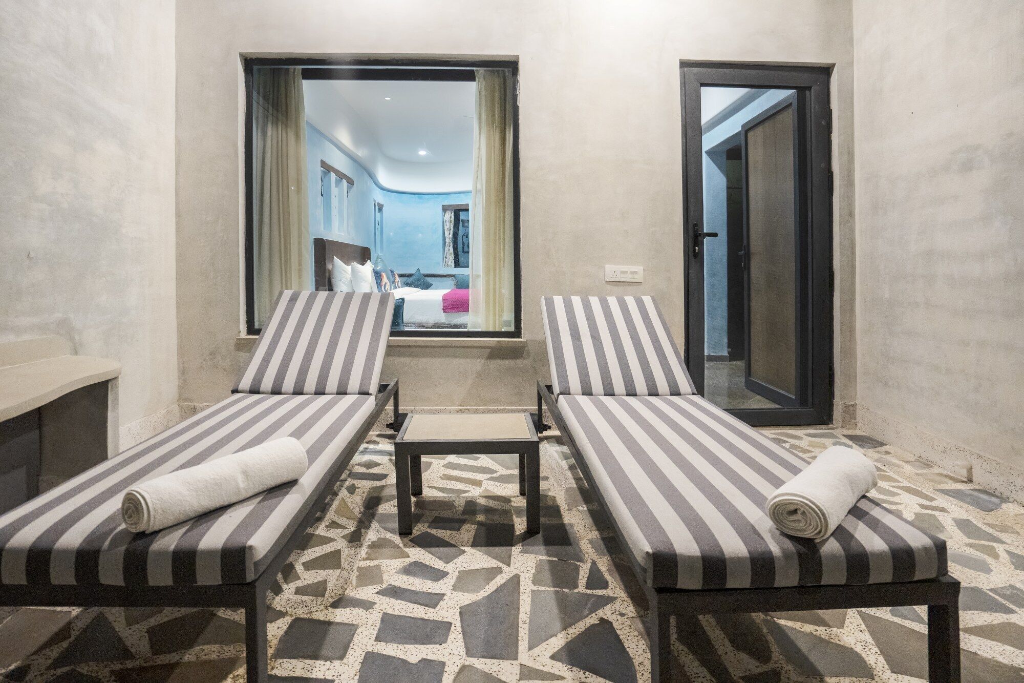 A spa room with two striped lounge chairs, a small table, and a patterned floor.