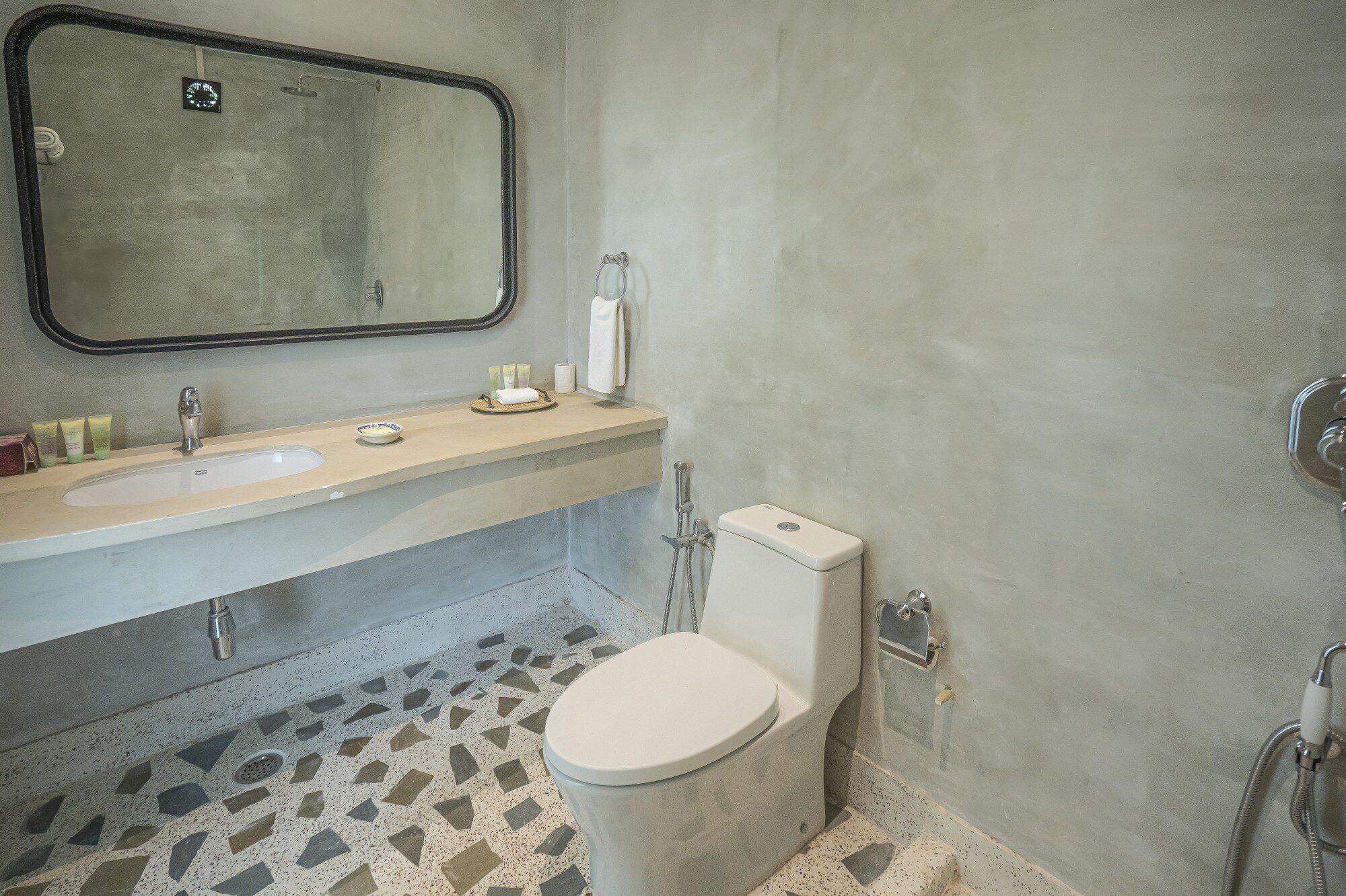 A bathroom with a sink, mirror, toilet, and a shower area.