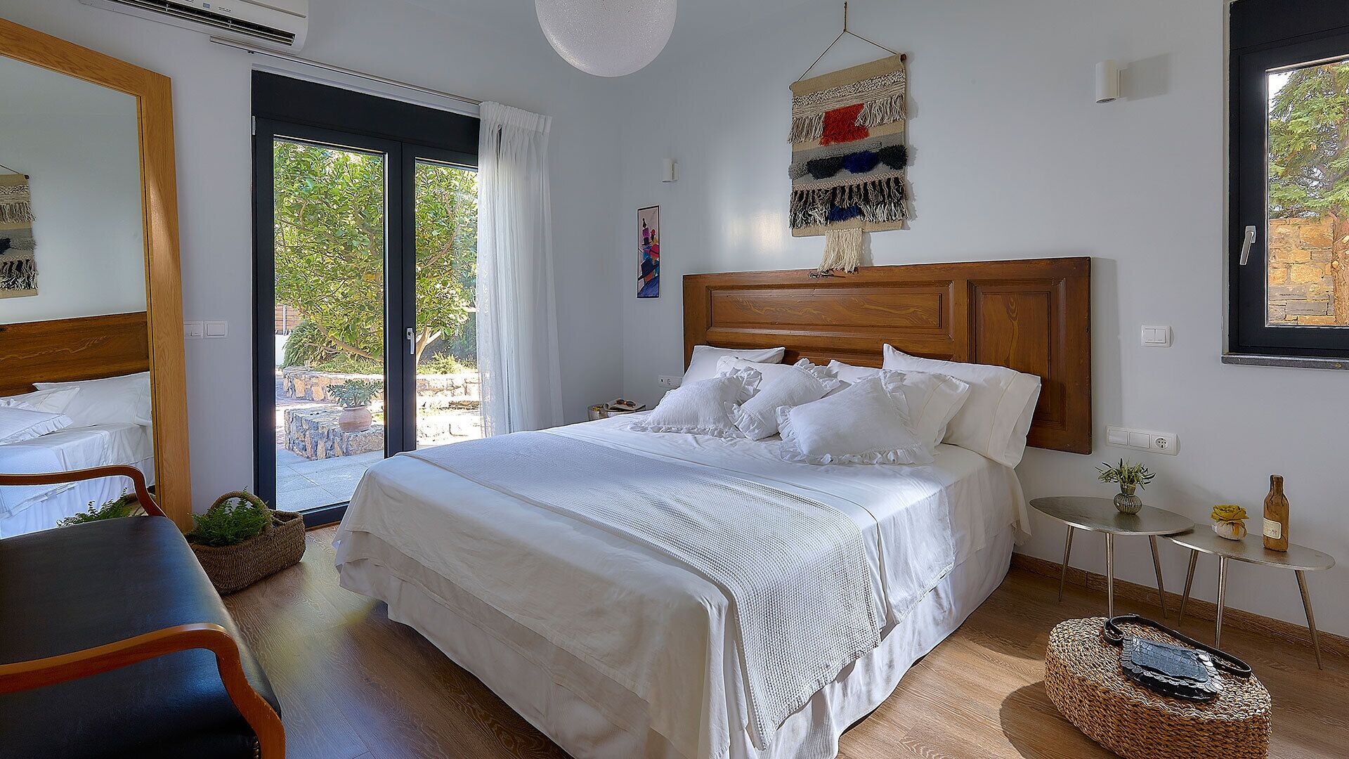 A bedroom with a large bed, a small table, a chair, and a view of the outdoors.
