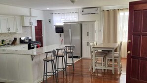Un'ampia cucina con mobili bianchi, un'isola centrale con sgabelli, un frigorifero e un tavolo da pranzo con sedie.