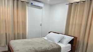 Un letto singolo con struttura in legno e coperta grigia in una stanza con pareti bianche e pavimento in legno.