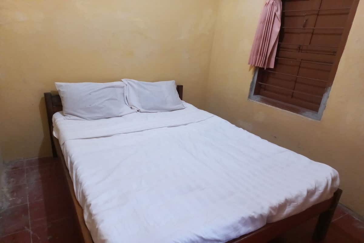 Una cama individual con ropa de cama blanca en una habitación con paredes amarillas y una ventana con persianas marrones.