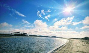 Una playa con un sendero arenoso, agua tranquila y cielo despejado.
