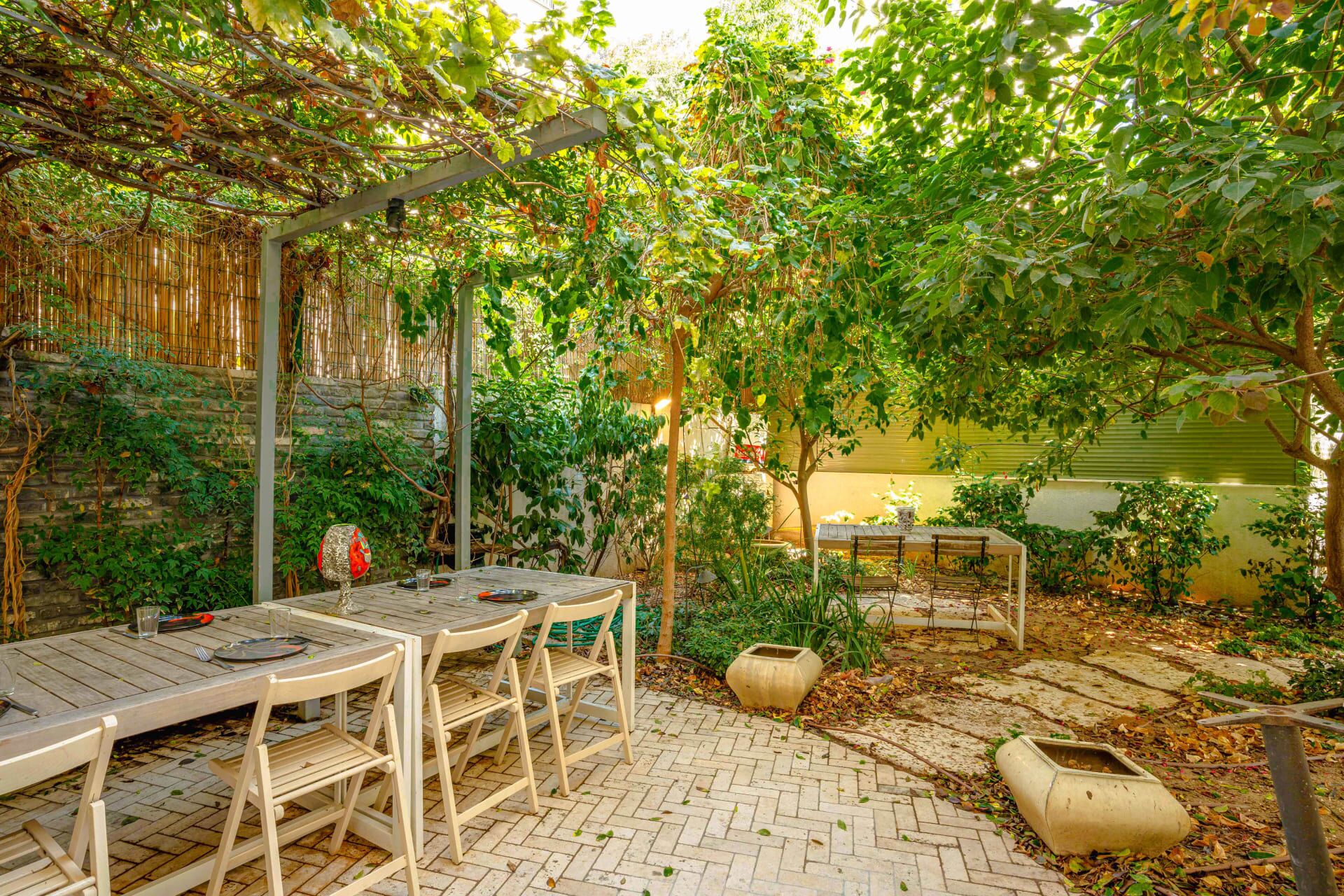 Une terrasse extérieure avec une table et des chaises, entourée d’une végétation luxuriante et agrémentée d’une pergola.