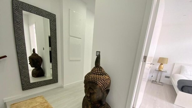 En moderne stue med en hvid sofa, en dekorativ Buddha-figur og et mønstret spejl på væggen.