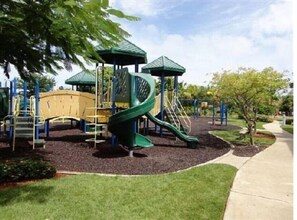 Children can play on the green slide and climb the structure in this playground area surrounded by a grassy lawn and paved walkway.