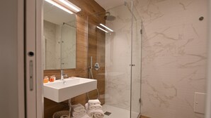 A modern bathroom with a glass-enclosed shower, a white sink with a mirror above, and neatly folded towels on a shelf. - Me too - Exclusive Apartments Studio Open Space Room 1 (BARI)