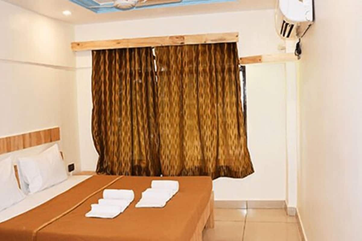 Quarto de hotel com cama, cabeceira de madeira, cortina e ar condicionado fixado na parede.