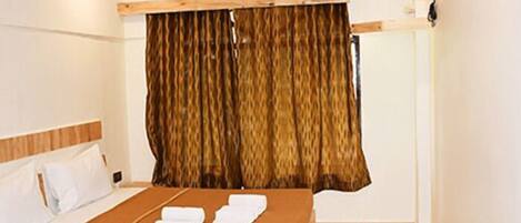 Habitación de hotel con cama, cabecera de madera, cortina y aire acondicionado instalado en la pared.