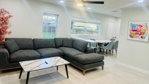 A modern living room with a sectional sofa, a coffee table, a dining table with chairs, and a ceiling fan. - 4 BR/2 BA walking distance to AT&T, Ranger Stadium, Texas Live, Six Flags (Arlington)