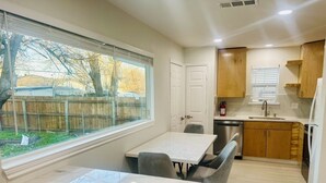 A modern kitchen with a dining area, wooden cabinets, and a large window overlooking a backyard. - 4 BR/2 BA walking distance to AT&T, Ranger Stadium, Texas Live, Six Flags (Arlington)
