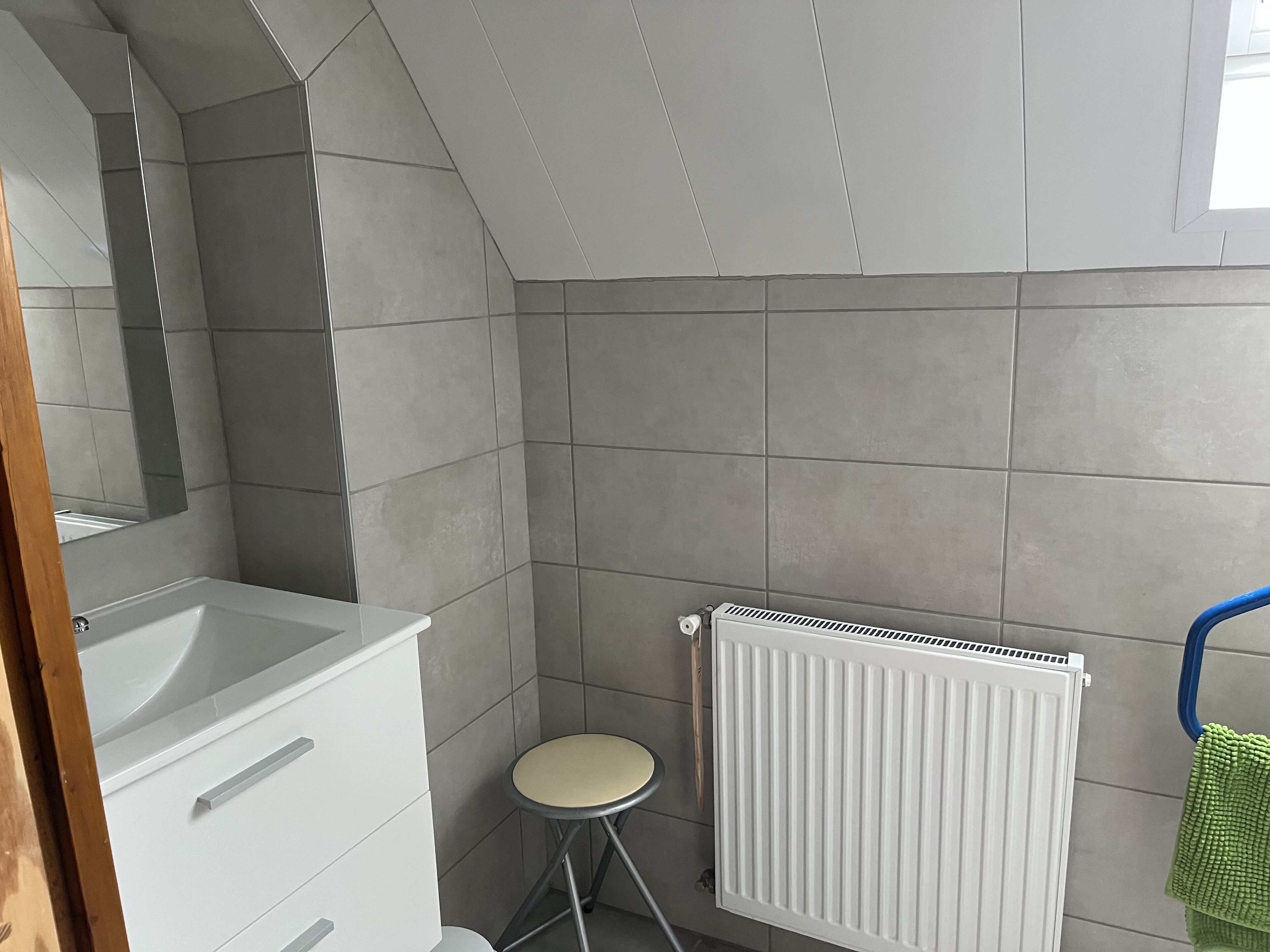 A bathroom with a white sink, a mirror, a radiator, and a green towel hanging on a blue towel rack.