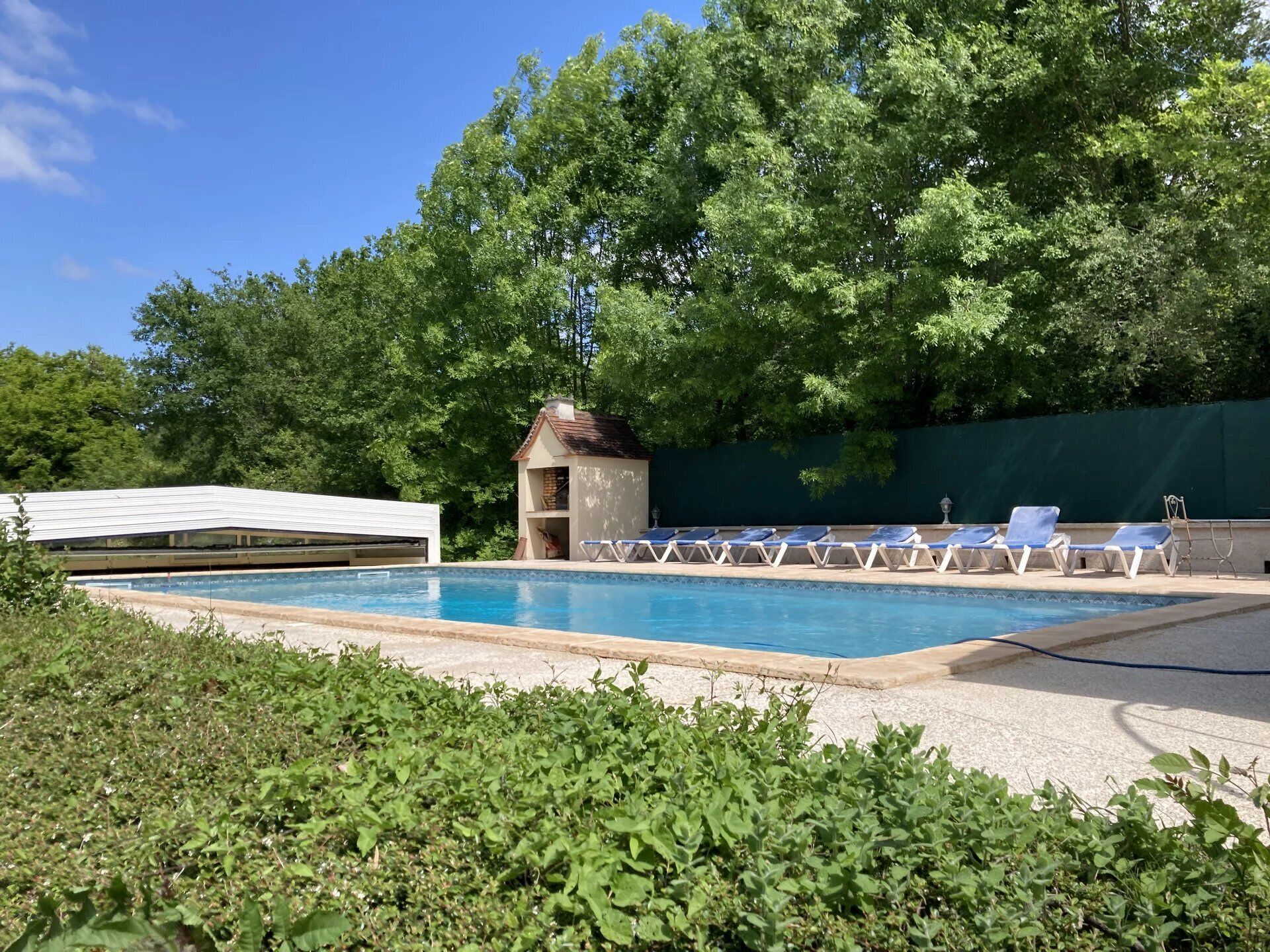 Une piscine entourée de chaises longues, un petit bâtiment et une végétation luxuriante.