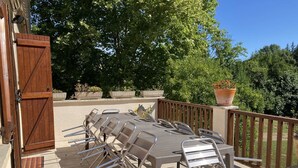 An outdoor patio with a long table and chairs, surrounded by potted plants and trees. - Les Costes, Calvignac. Large house with pool. Close to the river. (Calvignac)