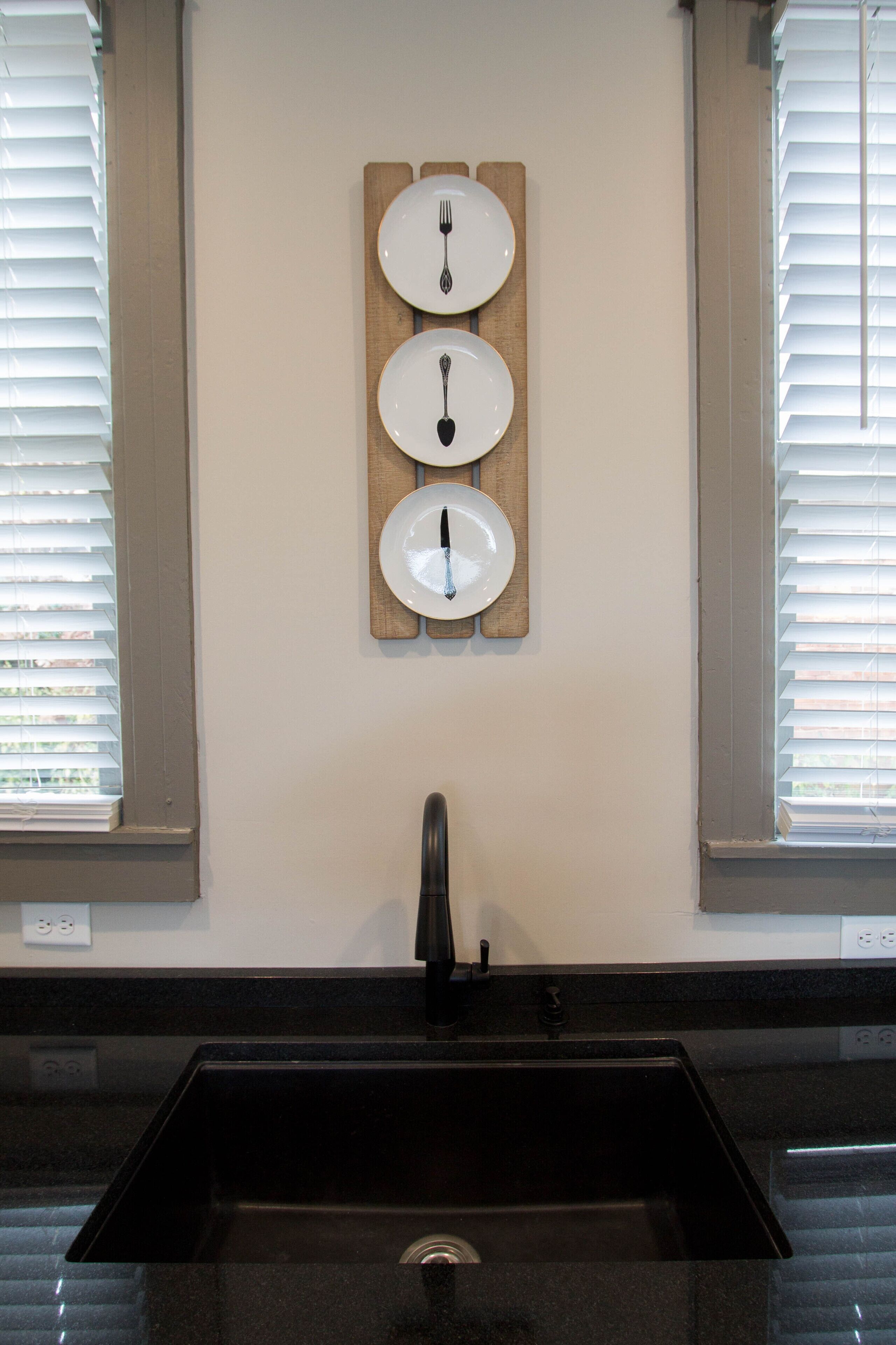 A kitchen with a black sink, a wooden wall-mounted plate rack, and a window with blinds.