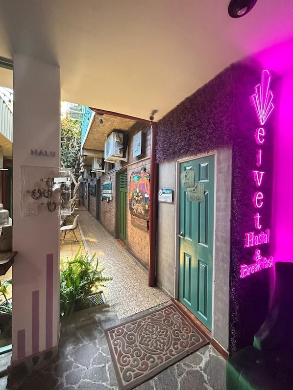 L’entrée d’un hôtel, avec une enseigne au néon, une porte verte et un paillasson à motifs.