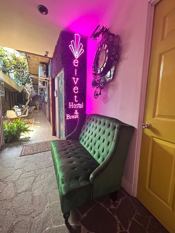 A green cushioned bench in a hallway with a neon sign reading "eivet Hostal & Break."