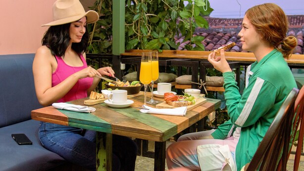 Two people dining at a wooden table with a view of a garden. - HOSTAL VELVET  (Santa Ana)