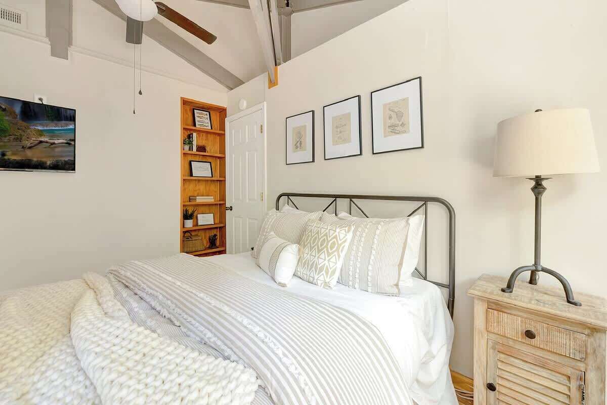Ein Schlafzimmer mit Bett, Nachttisch, Lampe, Bücherregal und gerahmten Bildern an der Wand.