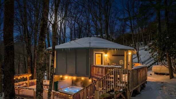 Eine Hütte mit Whirlpool, Holzterrasse und verschneiter Umgebung.