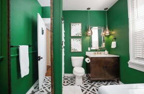 Ein Badezimmer mit grünen Wänden, einer weißen Toilette, einem Holzbadezimmermöbel und einem gemusterten Boden.