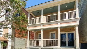 A two-story building with a balcony, a stone foundation, and a front door.