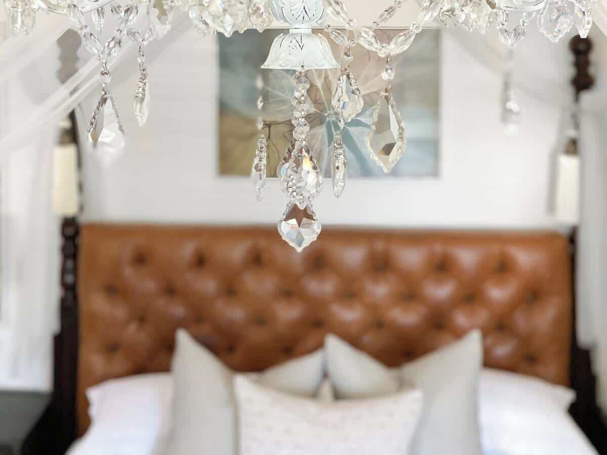 Une chambre à coucher avec une tête de lit capitonnée, un lustre en cristal suspendu et un tableau encadré au mur.
