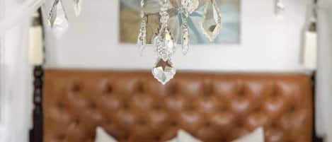 A bedroom with a tufted headboard, a hanging crystal chandelier, and a framed picture on the wall.