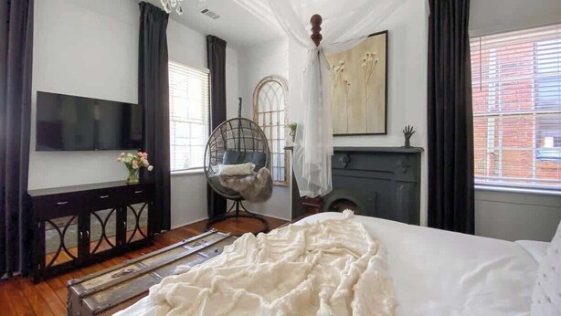 A bedroom with a bed, a chair, a TV, and a fireplace.