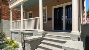 A two-story house with a front porch, a stone staircase, and a brick wall.