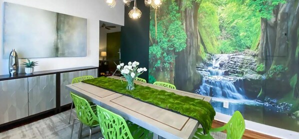 Ein moderner Essbereich mit einem langen Tisch, grünen Stühlen, einem Fellüberwurf und einem Wandgemälde mit Wasserfallmotiven.