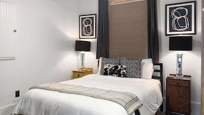 A bedroom with a bed, bedside tables, a dresser, and artwork on the walls. - Stylish Savannah Condo Steps to Forsyth Park (Savannah)