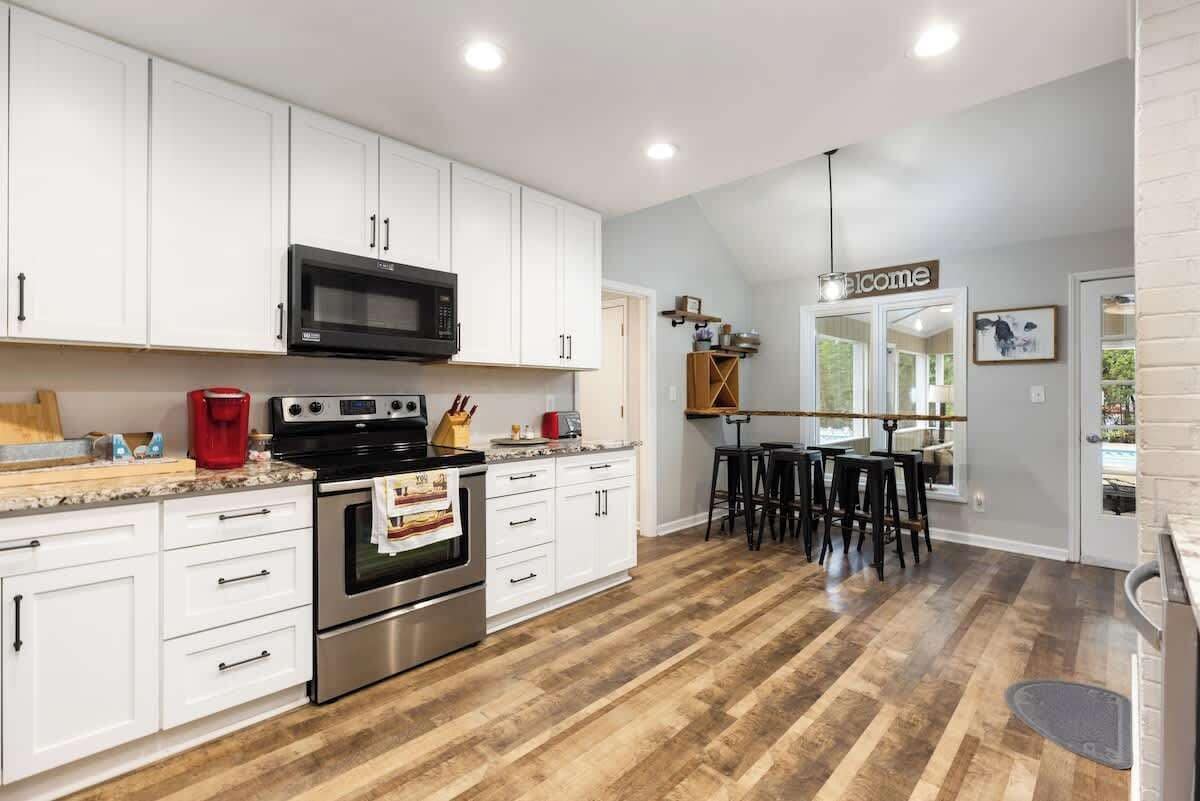 A modern kitchen with white cabinets, stainless steel appliances, and a wooden floor.
