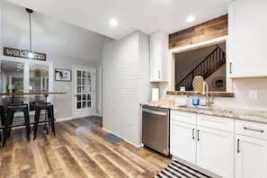 Une cuisine moderne avec des meubles blancs, un plancher en bois et un lave-vaisselle encastré.