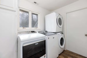 Une buanderie équipée d’un lave-linge et d’un sèche-linge à chargement frontal, d’une fenêtre située au-dessus du lave-linge et d’une porte sur le côté droit.