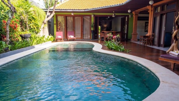 Una piscina con bordo curvo, circondata da un pontile in legno e rigogliosa vegetazione.