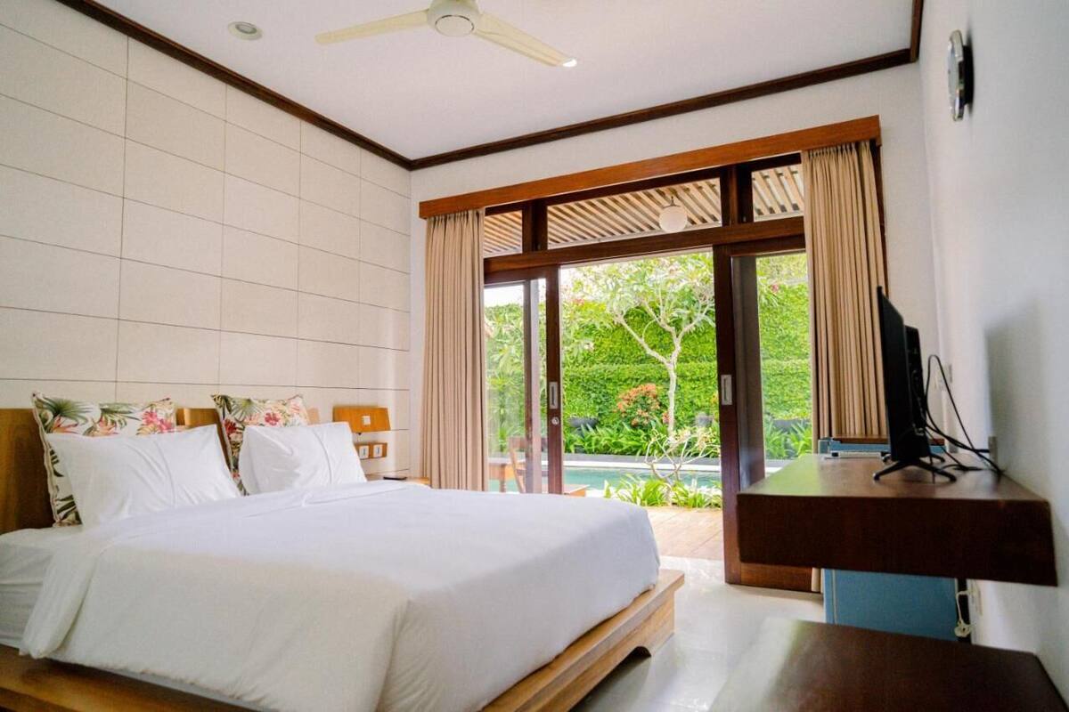 A hotel room with a large bed, a TV on a wooden stand, and a view of a garden through a sliding door.