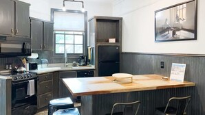 A modern kitchen with dark cabinetry, a central island with stools, a microwave, stove, and a refrigerator. - Charming Savannah Townhouse Walk to Forsyth Park  Downtown (Savannah)
