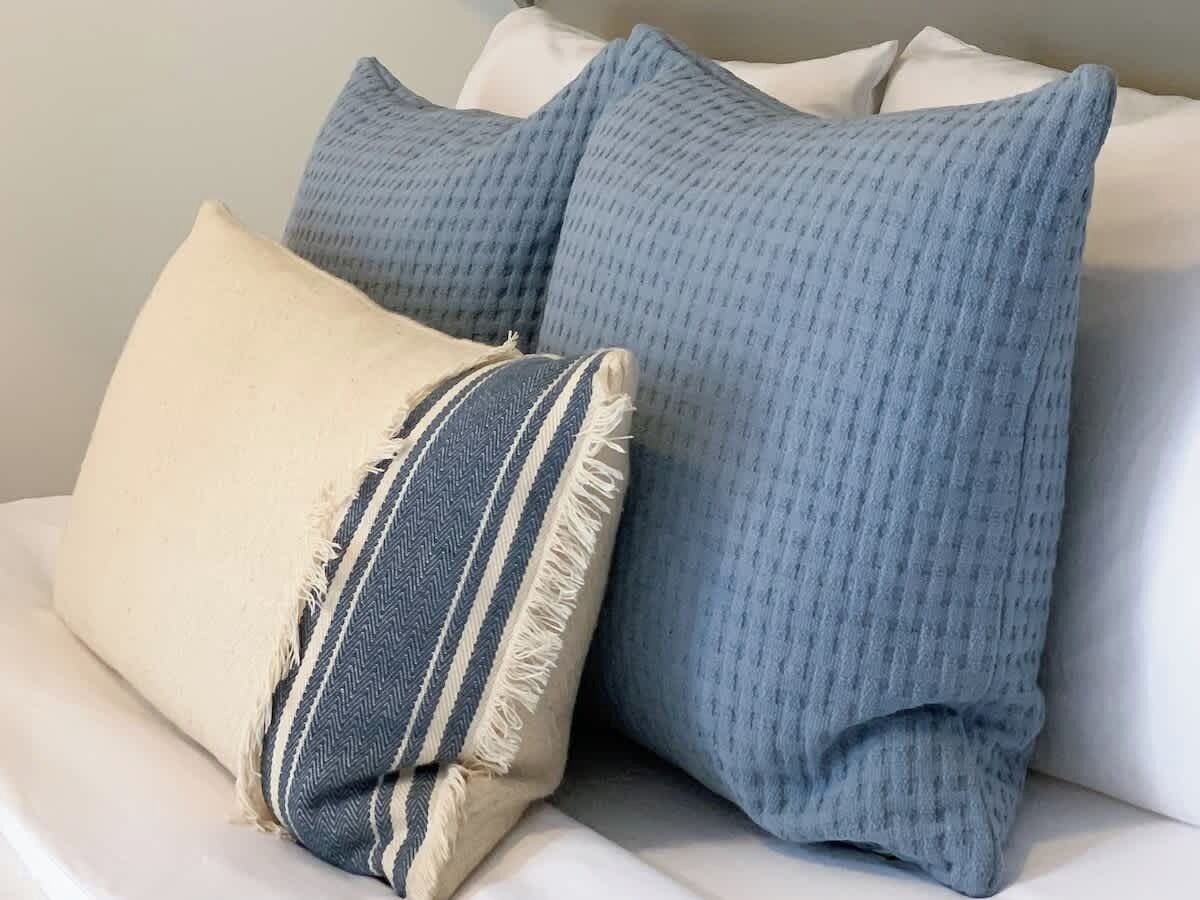 Ein weißes Sofa mit drei Kissen: ein beige, ein gestreiftes und ein einfarbig blaues.