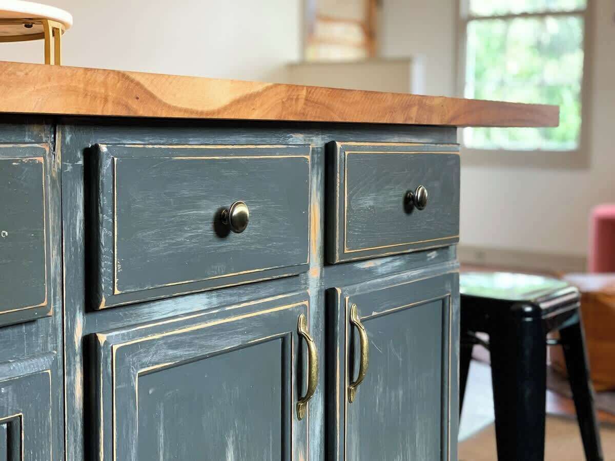 Une commode bleu foncé, dotée de poignées en laiton et d’un plateau en bois, avec de nombreux tiroirs et des portes.