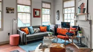 A living room with a grey sofa, orange armchair, and a television on a wooden stand. - Charming Savannah Townhouse Walk to Forsyth Park  Downtown (Savannah)