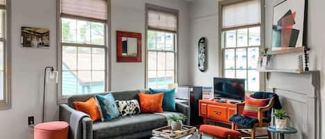 A living room with a grey sofa, orange armchair, and a television on a wooden stand.