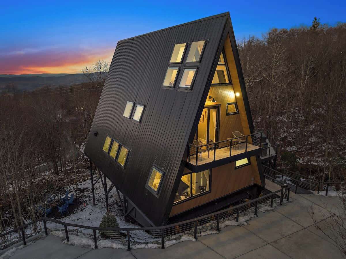 Een modern, hoekig huis met een opvallend schuin dak, grote ramen en een balkon.