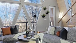 Een ruime loft-achtige kamer met een hoge plafond, grote ramen, en een gezellige zithoek met een bank en een ronde salontafel.