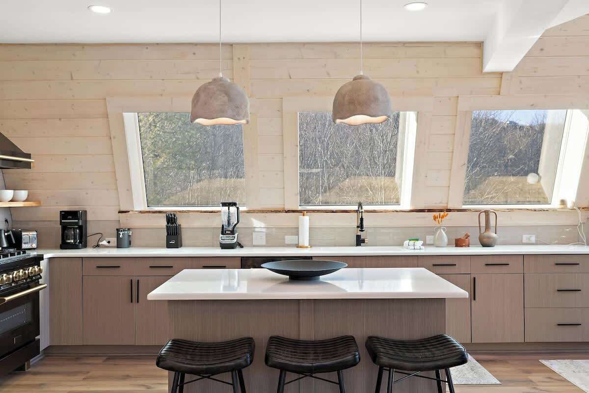 A modern kitchen with a central island, pendant lighting, and large windows.