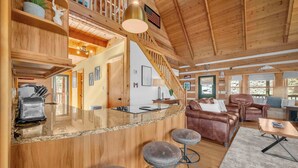 Un intérieur de cabine spacieux, avec un revêtement en bois, un coin cuisine, un espace salon comprenant un canapé et des fauteuils, et un escalier menant à un niveau supérieur.