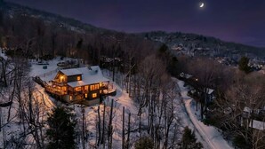 Un paysage enneigé, avec une cabane illuminée et un croissant de lune dans le ciel.